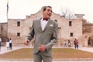 Pee-Wee Herman standing in front of the Alamo, with a sign for the “Crockett Hotel” in the background. (Your grade school teacher also probably didn’t tell you what racist monsters the “‘Merican heros” of the Alamo were. #LEARN)