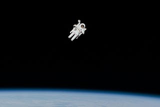 Astronaut EVA above Earth. The astronaut appears to be alone in the deep black of space, and only the implicit existence of the photographer suggests otherwise.