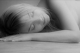 A young woman sleeps on a smooth grey floor.