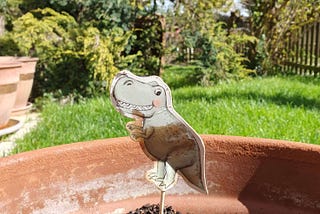 A paper dinosaur on a stick stuck into a plantless plant pot.