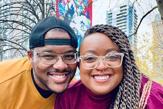 A young, Black couple smiling for the camera at Allan Gardens in Toronto, Canada