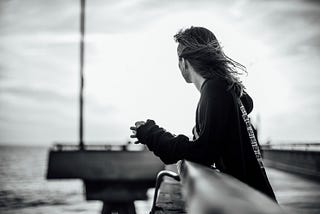 black and white photo of the author standing on a pier, looking out over the ocean