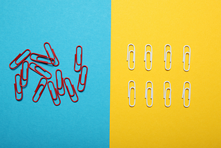 Sheet of paper split in two: blue side with scattered red paperclips and yellow side with neat rows of white paperclips.
