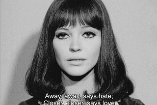 A screenshot from Jean-luc Godard’s Alphaville. A woman with shiny black hair and thick mascara stares into the camera. The subtitle reads: Away, away, says hate; Closer, closer, says love.