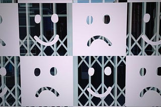 A shop window painted with alternating smiling faces and frowning faces, taken on the photo app Dispo.