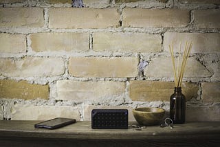 A photo from a wall with a little table in the front, where a smartphone, a bluetooth speaker and some decorations are placed on