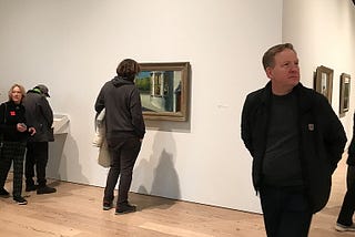 A handful of visitors at an exhibition of paintings.