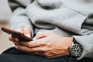 Image is a close up of a man texting. Only his hands and phone are visible and he’s wearing a wedding ring.