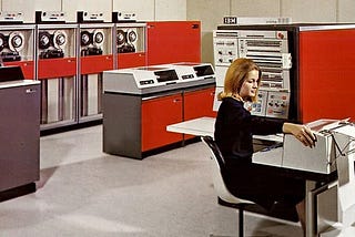 IBM System/360 promotional photo, ca. 1965. A woman sits at a terminal, surrounded by a System/360 with red panels.