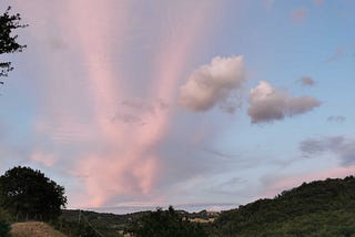 The pink clouds of sunset over a valley of green.