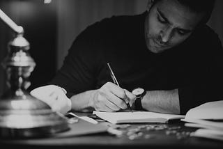 A black and white photo of a man writing notes in a journal