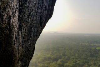 Dark stone wall over a horizon of lush green tropical trees.