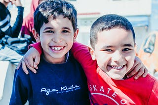 Two young boys smiling at the camera with arms around each other’s shoulders