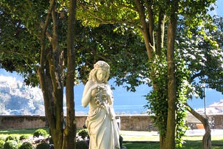 Statue of a female goddess surrounded by trees in a garden.