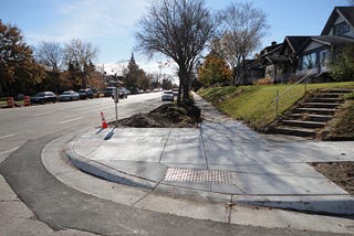 An image of a curb cut on the corner of a street. The sidewalk grades down to the street to allow for smooth crossing.