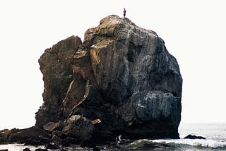 A man standing on a massive bolder at the waters edge.