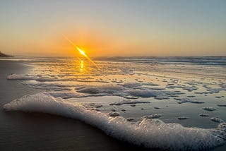 Sunrise over the Atlantic ocean in the background with sea foam in the foreground