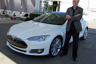 Elon Musk standing beside a Tesla