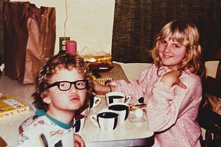 THe author at age seven with his sister, eleven, coloring easter eggs, looking into the camera.