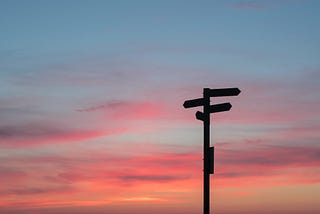 Directional signposts in shadow of a sunset