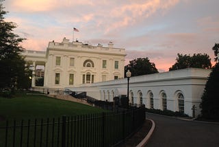 The US White House seen from the west with a sunset behind it.