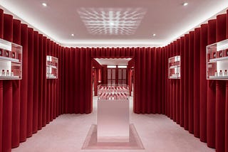 Glossier’s scene showroom has lilac carpeted floors and deep red velvet fabric covers the walls floor to ceiling.