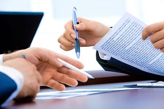 two sets of hands holding pens and documents