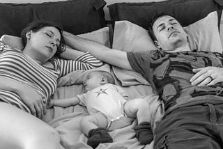 Black and white image of a mother, baby, and father sleeping in a bed