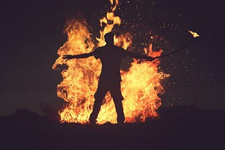 man in front of a bonfire, holding a stick with fire