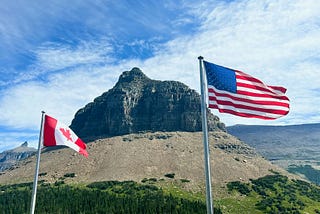Photo of a Canadian and American flag flying side by side in front of a mountain
