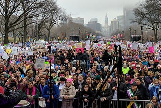 Latreice Branson of Drum Like a Lady looks out on a crowd of thousands of women and supporters on the Ben Franklin Parkway. Many of them are carrying signs and wearing pink pussy hats.
