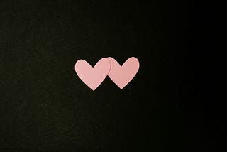 Two pink paper hearts on a black background
