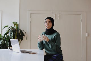 Woman in Hijab drinks coffee and gets ready to talk to users on her laptop