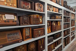 A series of bookcases filled with dozens of antique radios, most in wooden cabinets.