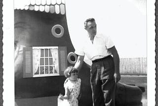 My Dad with his arm on my shoulder, standing in front of a giant shoe at a theme park, circa 1960.