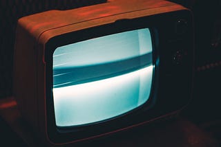 Older wood encased box television with a gray distorted screen sitting in a dark room.