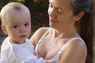 Parent holding baby and looking lovingly at baby, both wearing white.