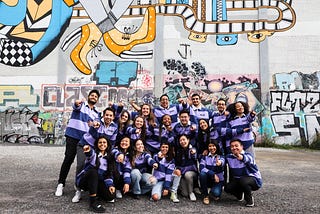 19 people in matching jersey posing in front of a grafitti wall