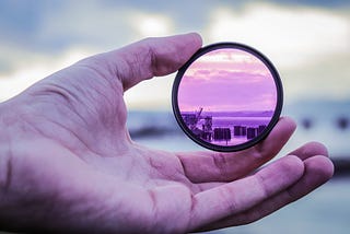 A hand holding up a lens over a blurry image of a landscape