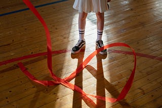 A girl in a gymnasium, twirling an athletic ribbon.