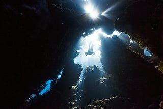 A figure diving deep into the ocean through rocks