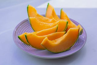 A plate of freshly sliced cantaloupe melon on a light background, representing the hidden food safety risks of cut melons, which can harbor bacteria like Salmonella if not properly handled or refrigerated.