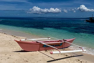 pink bangka boat with two outriggers on sand, with the turquoise water behind it