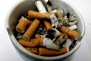 A circular ceramic ashtray that is filled with cigarette ends.
