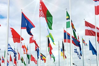 World flags from many countries against a cloudy sky.