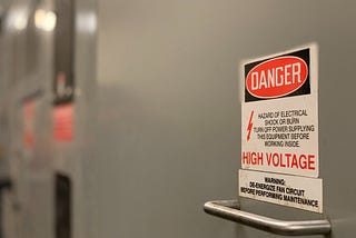 A high voltage sticker above the handle of grey equipment.