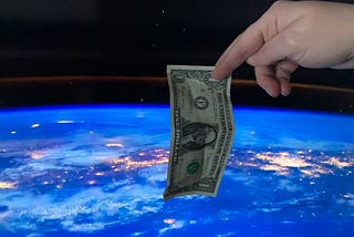 A dollar bill being held above a picture of the Earth