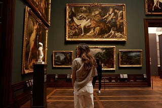 A woman standing in an art gallery looking at paintings