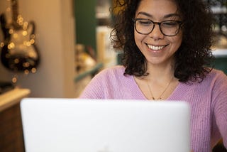A woman smiles at her laptop screen.