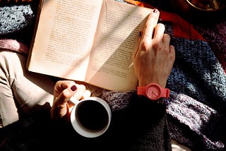 A woman reading a book with a cup of coffee.